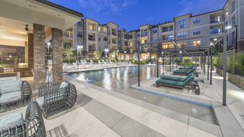 A swimming pool with lounge chairs in front of an apartment building